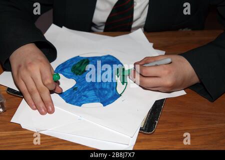 Ein britischer vorjugendlicher Schuljunge in Uniform zeichnet ein Bild von Planet Erde mit Filzstiften, Kinderzeichnung der Erde Stockfoto