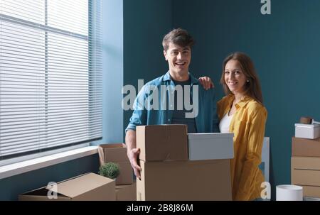 Fröhliches junges Paar posiert in ihrem neuen Haus und hält Kartonboxen: Heimverlagerungskonzept Stockfoto