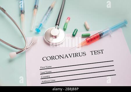 Eine Spritze mit einem Bluttest und ein Stethophonendoskop mit Ein Patientenfragebogen und Tabletten für eine Pandemie eines Cornovirus Stockfoto