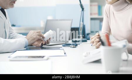 Professioneller Oberarzt, der einen Patienten im Büro betagt und ein verschreibungspflichtiges Medikament gibt Stockfoto