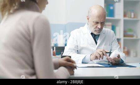 Professioneller Oberarzt, der einen Patienten im Büro betagt und ein verschreibungspflichtiges Medikament gibt Stockfoto