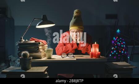 Gestresste Geschäftsfrau, die am späten Abend am Heiligabend im Büro gefriert, arbeitet und denkt mit Kopf in den Händen Stockfoto