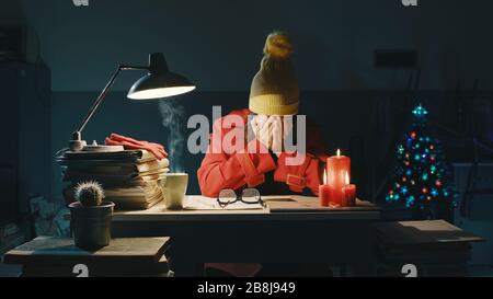 Gestresste Geschäftsfrau, die am späten Abend am Heiligabend im Büro gefriert, arbeitet und denkt mit Kopf in den Händen Stockfoto