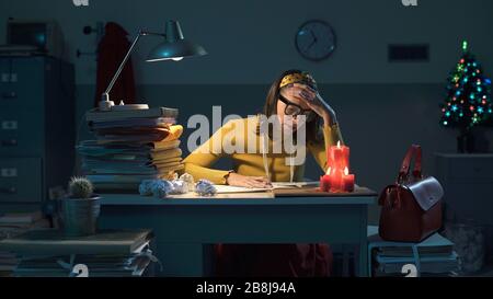 Eine effiziente Sekretärin, die spät am Abend im Büro an Heiligabend arbeitet, führt schwierige Berechnungen durch Stockfoto