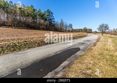 Alte Asphaltstraße in der Nähe des Feldes. Tschechische Landschaft. Landstraße in der Nähe des Waldes. Frühlingmorgen auf der Landstraße. Stockfoto