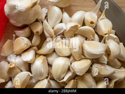 Viele Knoblauchzehen schließen sich mit einem Messer auf einer Holzschneideplatte an. Stockfoto