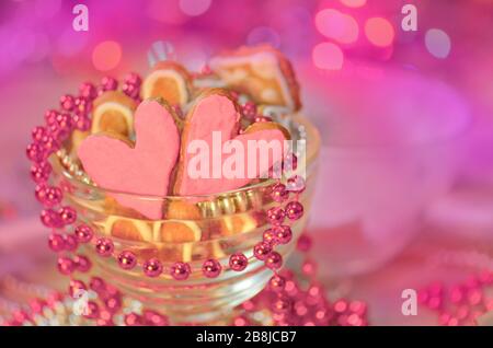 Valentinskekse mit Herzform. Rosa Herzkekse auf rotem Stoffhintergrund. Zwei Herzen Plätzchen gebacken Valentinstag Stockfoto