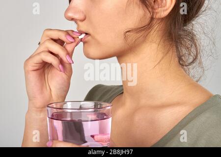 Junge Frau, die Pille nimmt und einen Glasbecher hält. Stockfoto