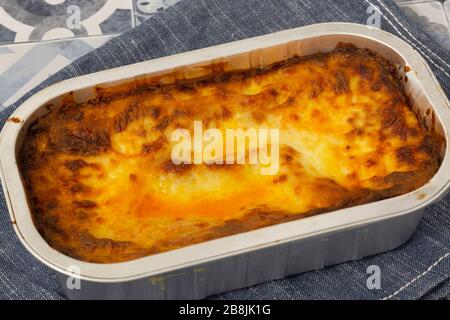 Beef Lasagne oder Lasagne zubereitete, tiefgefrorene Mahlzeit, die in einem Metallbackblech auf einem blauen Teehandel zubereitet wird. Fast-Food-Konzept Stockfoto