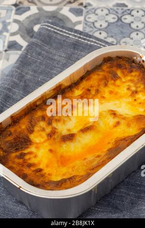 Beef Lasagne oder Lasagne zubereitete, tiefgefrorene Mahlzeit, die in einem Metallbackblech auf einem blauen Teehandel zubereitet wird. Fast-Food-Konzept Stockfoto