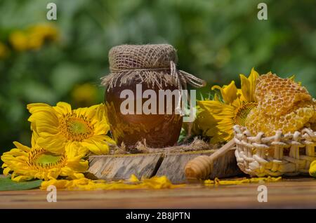 Honig mit Honigabipper auf Holztisch. Organischer Blumenhonig vor verschwommenem Hintergrund mit Blumen Stockfoto