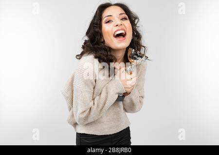 Das brünette Mädchen in einem weißen Pullover hält ein Retro-Mikrofon in der Hand und singt ein Lied auf weißem Hintergrund Stockfoto