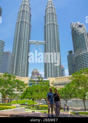 Touristenpaar im KLCC Park vor den Petronas Twin Towers und Suria KLCC Shopping Mall Kuala Lumpur Malaysia. Stockfoto