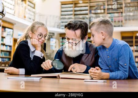 Konzentrierter Professor für ältere Menschen und seine zwei kleinen cleveren niedlichen Schüler, die gemeinsam Buch lesen. Großvater und neugierige Enkel Junge Stockfoto