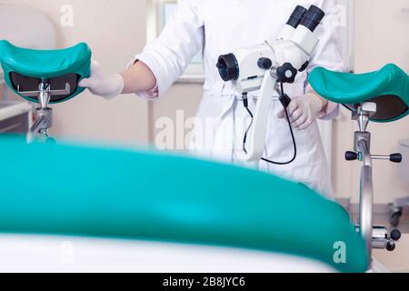 Gynäkologischer Raum mit Stuhl und Ausstattung. Hände weiblicher Ärzte mit Werkzeugen zur Untersuchung der Gesundheit von Frauen. Stockfoto