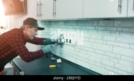 Portrait von ernsten Mann in Uniform steht drinnen, mit einer Bohrmaschine und der Installation der neuen Steckdose in der Wohnung. Horizontale erschossen. Seitenansicht Stockfoto