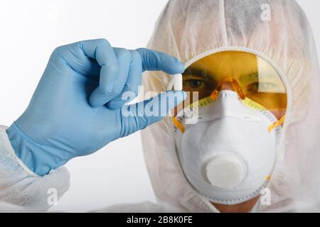 Ein Arzt in einem Einweg-Antiepidemianzug mit einer Schutzmaske und einer Brille hält die Tablette auf weißem Hintergrund Stockfoto