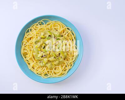 Spaghetti mit einer cremefarbenen Sauce mit Zucchini und Lauch in hellblauer Platte auf weißem Grund von oben. Stockfoto