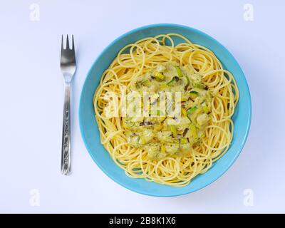 Spaghetti mit einer cremefarbenen Sauce mit Zucchini und Lauch in hellblauer Platte auf weißem Grund von oben. Stockfoto