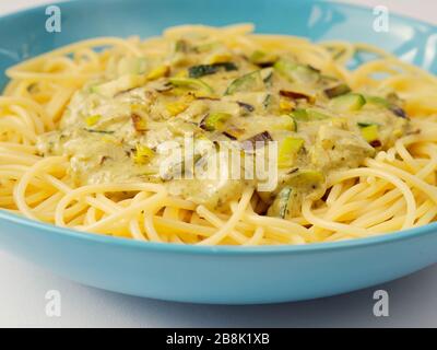 Spaghetti mit einer cremefarbenen Sauce mit Zucchini und Lauch in hellblauer Platte auf weißem Grund. Stockfoto