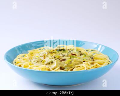 Spaghetti mit einer cremefarbenen Sauce mit Zucchini und Lauch in hellblauer Platte auf weißem Grund. Stockfoto