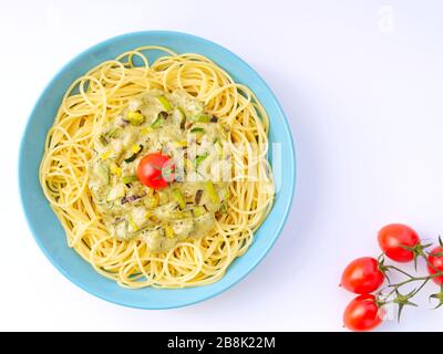 Spaghetti mit einer Sahnesauce mit Zucchini und Lauch mit einigen Tomaten zur Dekoration in einem hellblauen Teller auf weißem Hintergrund von oben. Stockfoto