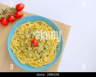 Spaghetti mit einer Sahnesauce mit Zucchini und Lauch mit einigen Tomaten zur Dekoration in einem hellblauen Teller auf weißem Hintergrund von oben. Stockfoto