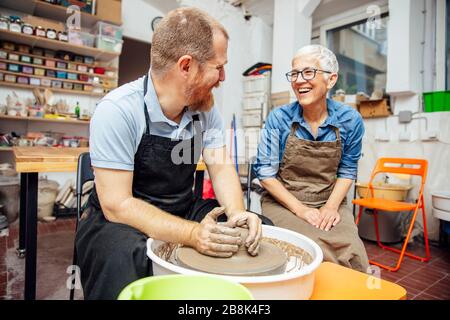 Ältere Frau spinnen Ton auf einem Rad mit Hilfe eines Lehrers an Keramik Klasse Stockfoto