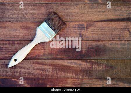 Holzbretter mit Fleckenansicht von oben. Eine Bürste mit Holzgriff und natürlichen Borsten vor dem Hintergrund bemalter Holzbohlen. Malen Stockfoto