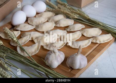 Knödel mit Eiern und Kartoffeln an Bord. Zutaten für Pelmeni-Zwiebeln, Arugula, Eier, Lorbeerblatt Stockfoto