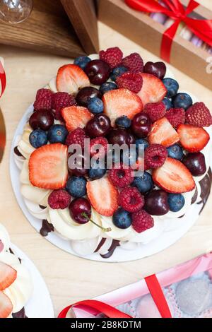 Pavlova-Kuchen mit frischen Erdbeeren, Kirschen, Blaubeeren und Himbeeren, geschmolzene Schokolade und Schlagsahne. Stockfoto