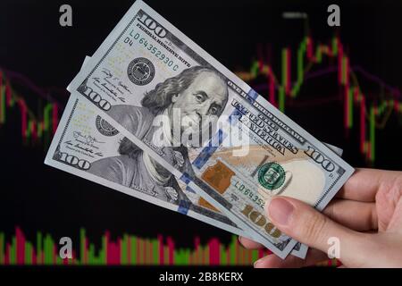 Hände, die Dollar vor einem Laptop-Monitor mit einem Kursdiagramm halten.Forex und trading.A Händler handeln Aktien, Anleihen und Wertpapiere oder Währungen auf t Stockfoto