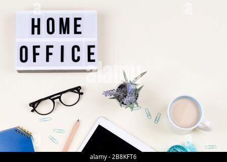 Leuchtkasten mit TEXT-HOME OFFICE mit Notizbuchbleistiftbrille Blumen und Tee. Copy-Bereich Coronavirus, europa Stockfoto