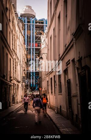 Leute, die eine traditionelle Pariser Hinterstraße mit den postmodernen Pfeifen und Schloten des Centre Pompidou im Hintergrund, Paris, Frankreich, entlang gehen Stockfoto