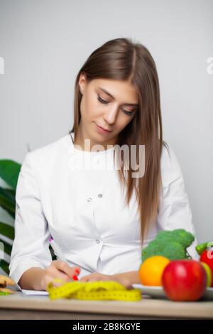 Frau im weißen Mantel Ernährungsberater schreibt ein gesundes Diätprogramm für Gewichtsverlust Stockfoto