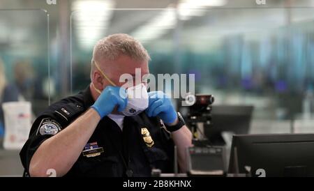 Ein US-amerikanischer Zoll- und Grenzschutzbeamter passt seine Gesichtsmaske an, bevor er internationale Passagiere, die am Dulles International Airport am 13. März 2020 in Dulles, Virginia ankommen, einer Überprüfung vorstellt. Als Reaktion auf die COVID-19 haben die pandemischen CBP-Beamten und Reisenden mit Coronavirus begonnen, Handschuhe und Masken als Schutz vor viraler Belastung zu tragen. Stockfoto