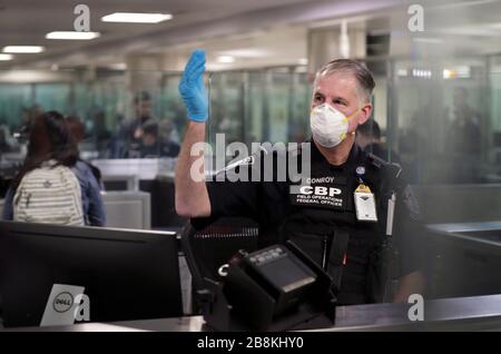 Ein US-amerikanischer Zoll- und Grenzschutzbeamter schirmt internationale Passagiere ab, die am Dulles International Airport ankommen und persönliche Schutzausrüstung tragen, 13. März 2020 in Dulles, Virginia. Als Reaktion auf die COVID-19 haben die pandemischen CBP-Beamten und Reisenden mit Coronavirus begonnen, Handschuhe und Masken als Schutz vor viraler Belastung zu tragen. Stockfoto