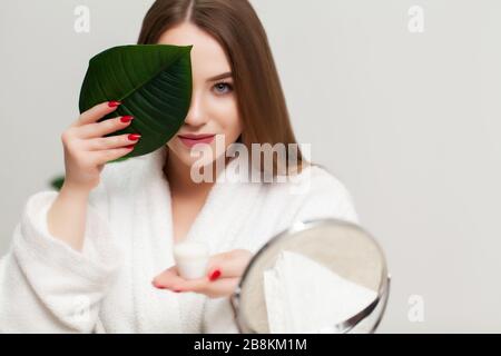 Hübsche junge Frau, die im Bad eine Creme zur Pflege des Gesichts hält Stockfoto