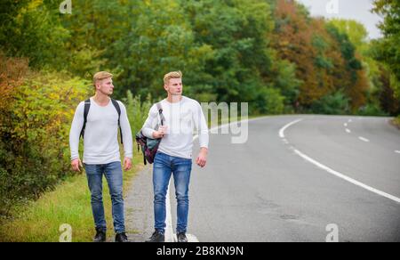 Fahren Sie in der Nähe des Stadtrandes. Reisende auf dem Weg. Freunde, die hitchhitchhamps unterwegs Firmenfreunde Reisende, die auf dem Naturhintergrund der Straße hitchwandern. Beginnen Sie mit dem Wandern ein tolles Abenteuer in Ihrem Leben. Stockfoto