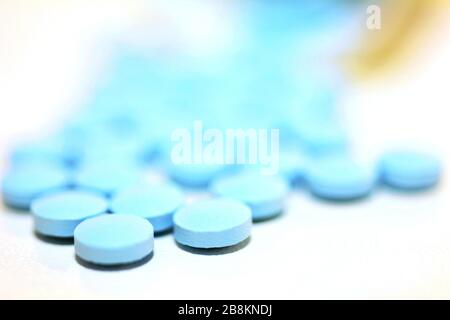 Nahaufnahme einer blauen Drogenpille, die aus einer Flasche auf dem weißen Hintergrund verschüttet wird. Stockfoto