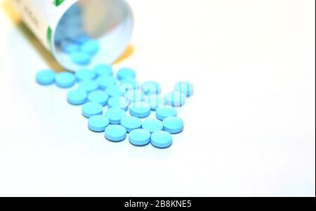 Nahaufnahme einer blauen Drogenpille, die aus einer Flasche auf dem weißen Hintergrund verschüttet wird. Stockfoto