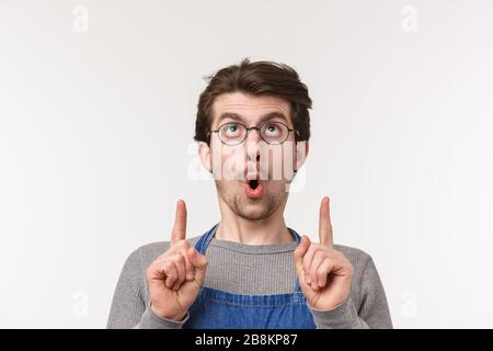 Nahaufnahmen von interessiertem und aufgeregtem kaukasischem bärtigen Kerl in Schürze und Brille sagen Wow und Stare zeigen die Finger auf etwas kühles, Fleck Stockfoto