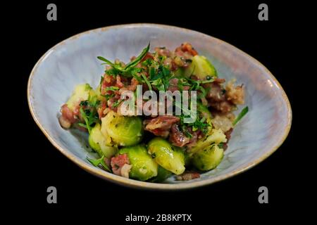 Rosenkohl mit Rinderspeck in einer Servierschale mit schwarzem Hintergrund Stockfoto