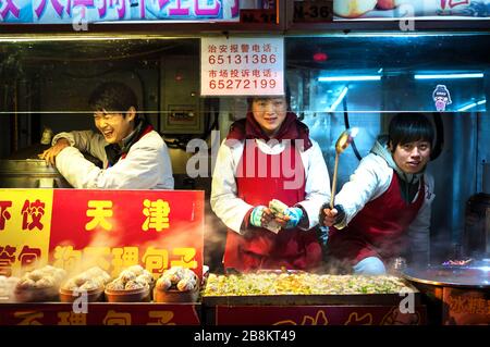 WANGFUJING NACHTMARKT, PEKING - 25. DEZ 2013 - Junge Imbissverkäufer genießen sich in der Wangfujing Imbissstraße, Peking Stockfoto