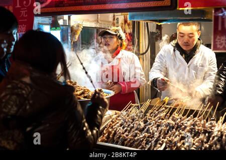 WANGFUJING NACHTMARKT, PEKING - 25. DEZ 2013 - Imbissverkäufer, die seltsames Fleisch auf Stöcken in der Wangfujing Imbissstraße, Peking, verkaufen Stockfoto