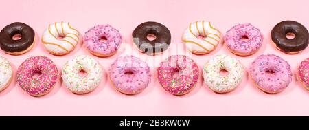 Doughnuts mit mehrfarbiger Glasur in zwei Reihen auf trendigen pinkfarbenen Hintergrund. Donuts sind traditionelle süße Gebäckstücke. Kreatives Webbanner. Stockfoto