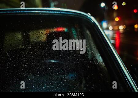 Altauto-Nahaufnahme, Regentropfen an der Windschutzscheibe, farbige Seite, Nacht, Abend Stockfoto