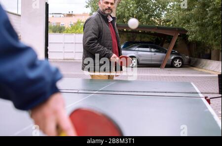 Glücklicher reifer Mann und sein Sohn spielen im Freien Tischtennis wegen COVID 19, Coronavirus Stockfoto