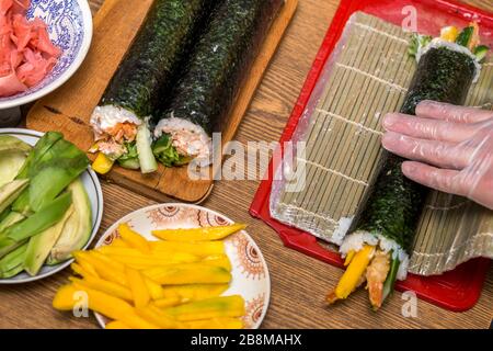 Die Sushi und Rollen zu Hause. Platten mit Zutaten für traditionelle japanische Küche und Sushi Rollen auf Holzbrett am Küchentisch, Ansicht von abov Stockfoto