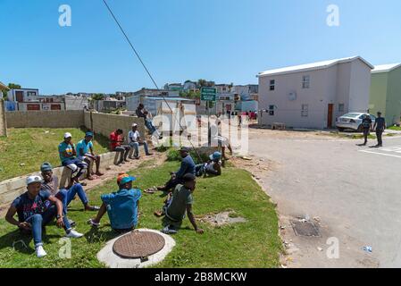 Zwelihle, Hermanus, Westkappo, Südafrika. Junge Männer, die am Straßenrand sitzen und auf der Suche nach Arbeit in der Gemeinde Zschweihle in Hermanus, Westkappo, sind. Stockfoto